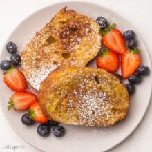 overhead view air fryer french toast on a plate, sprinkled with powdered sugar and surrounded with berries.