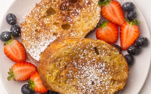 overhead view air fryer french toast on a plate, sprinkled with powdered sugar and surrounded with berries.