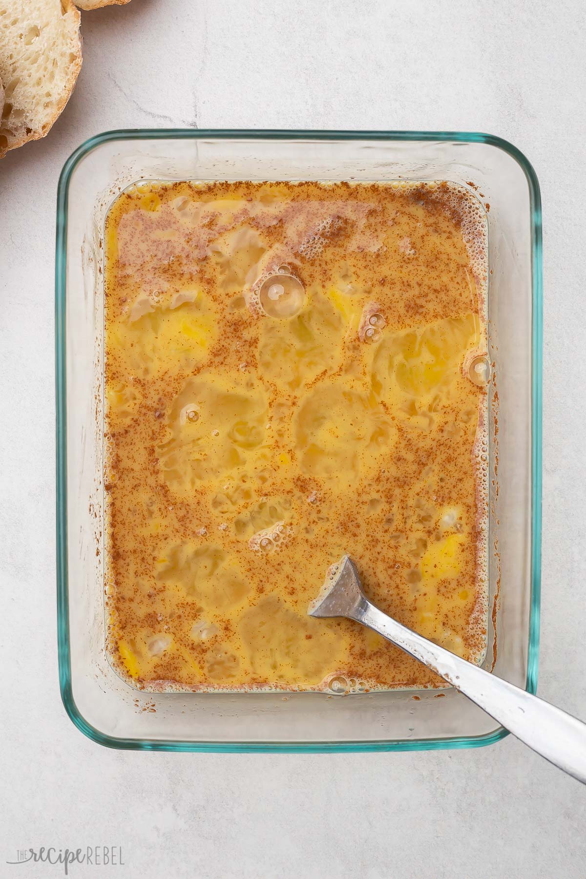 a glass dish and fork with french toast ingredients mixed in it.