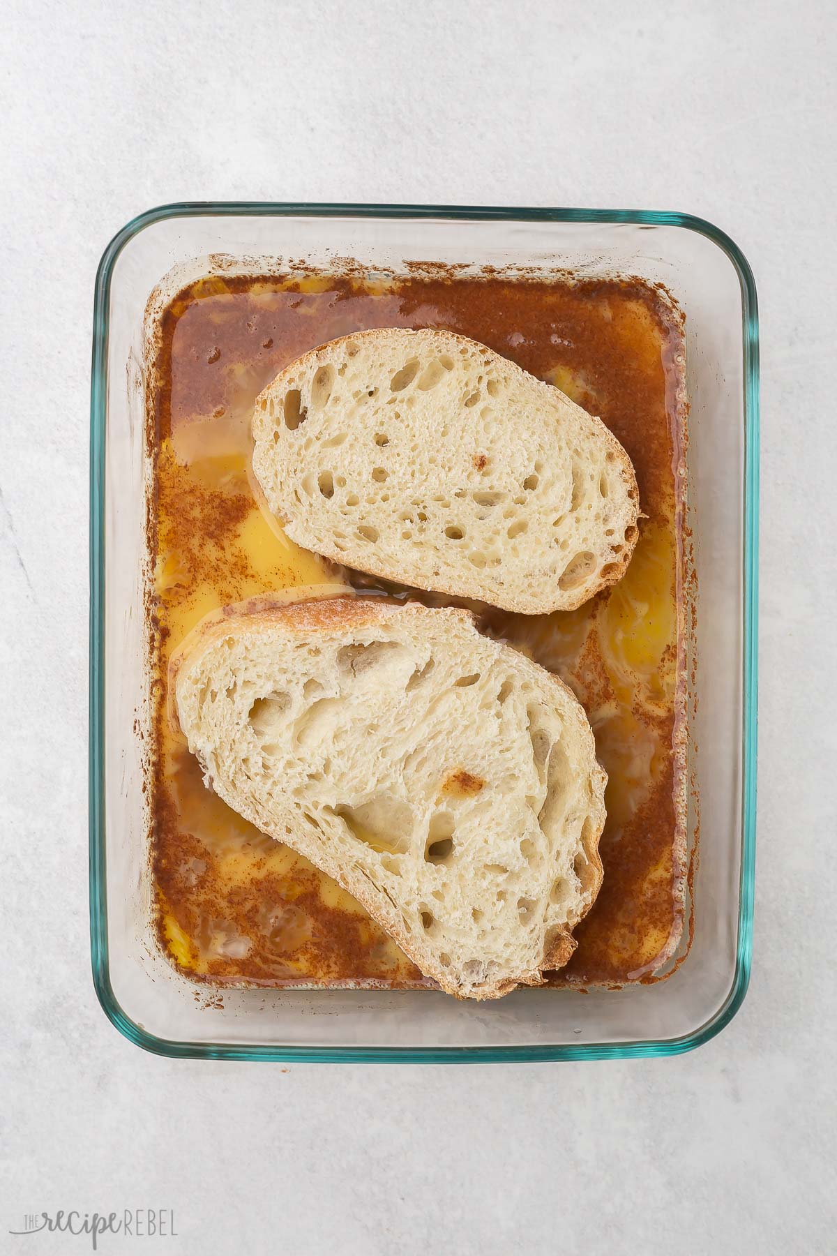 two pieces of bread laying in a glass dish with french toast wet ingredients.
