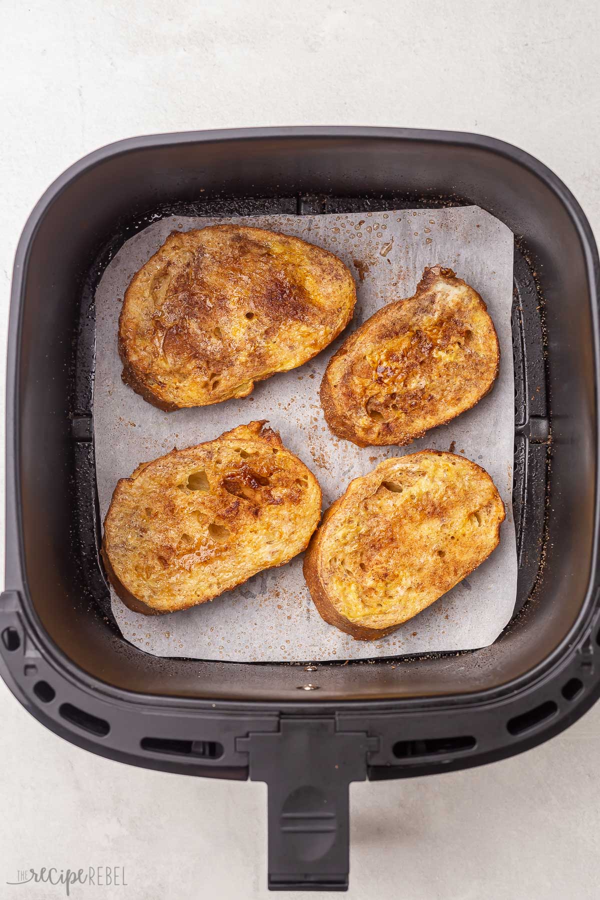 four pieces of fried french toast lying on parchment paper in air fryer basket.