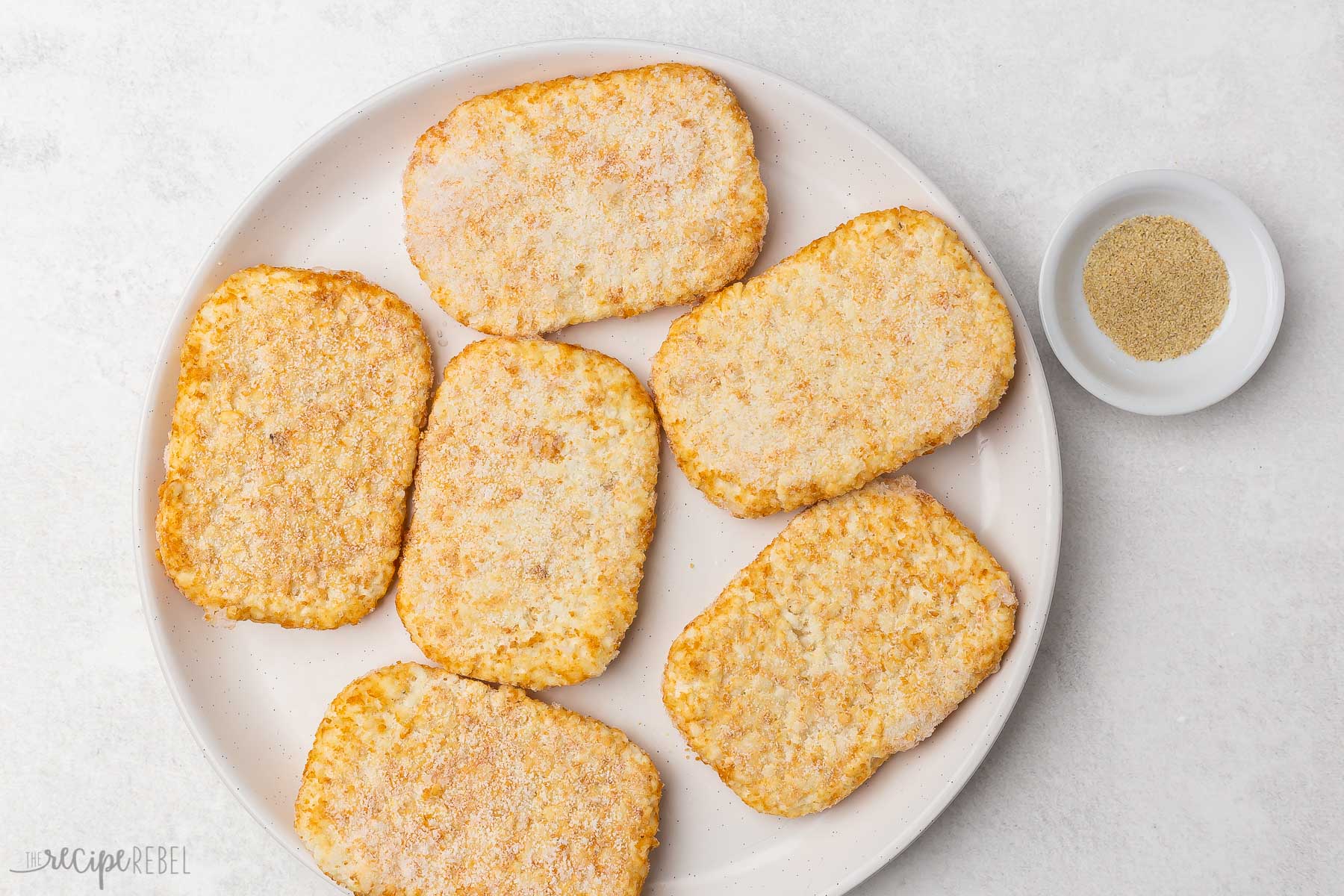 frozen hash brown patties on a white plate with small bowl of seasoning beside.