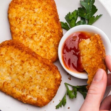 air fryer hash brown patty being dipped into ketchup bowl.