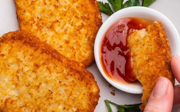 air fryer hash brown patty being dipped into ketchup bowl.