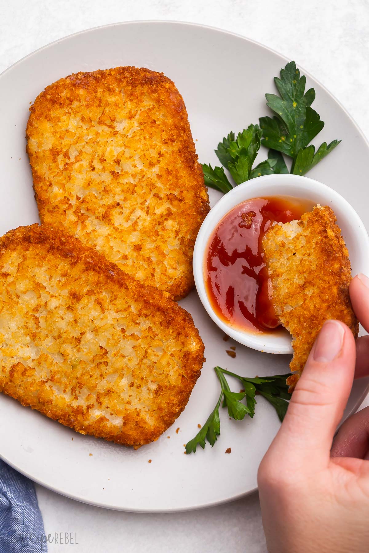 air fryer hash brown patty being dipped into ketchup bowl.