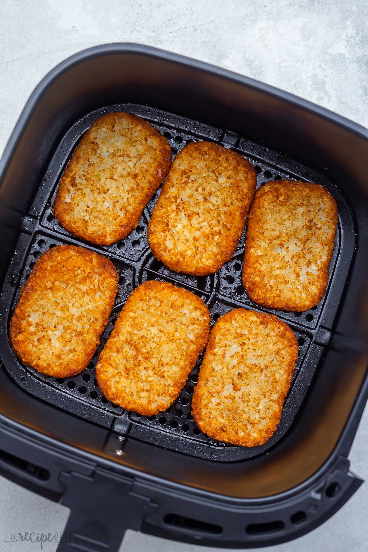 overhead view of golden hash brown patties lying in black air fryer basket.