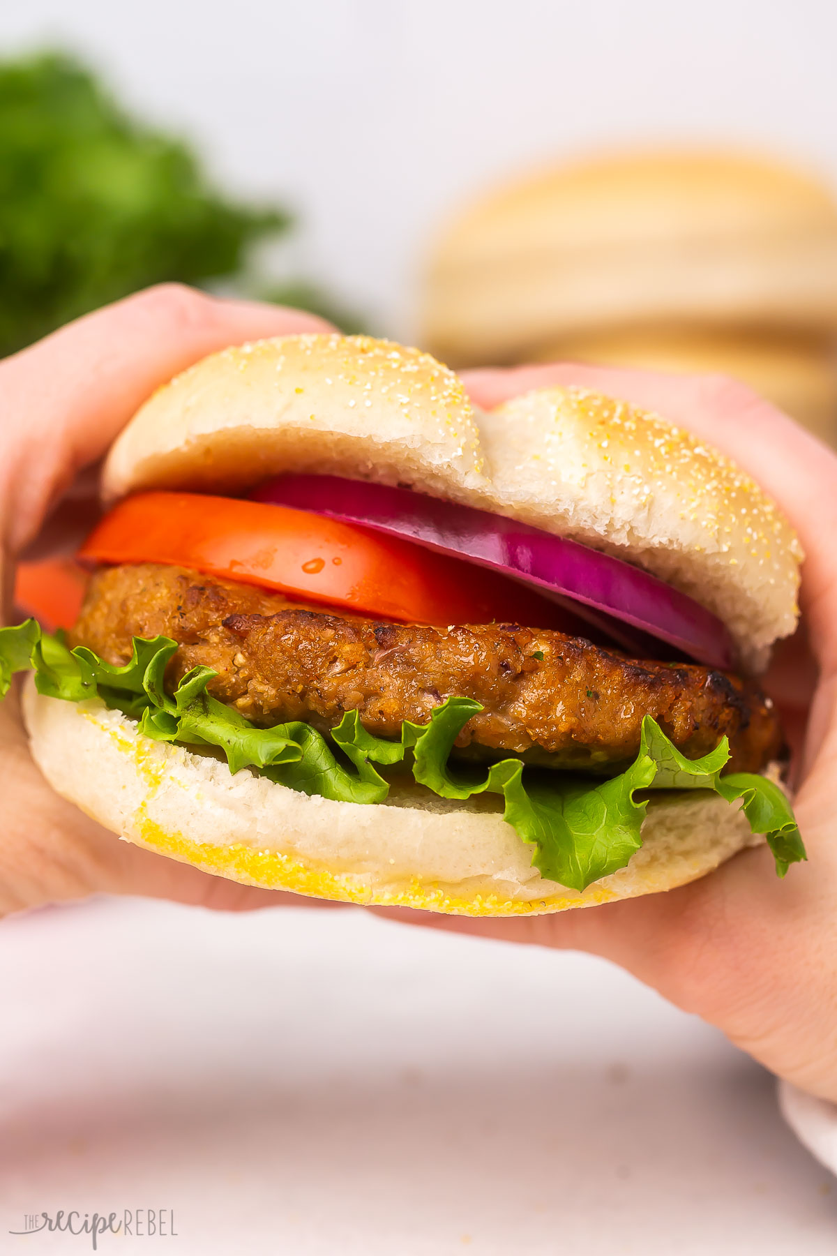 Close up of two hands holding turkey burger with lettuce and buns in the background.
