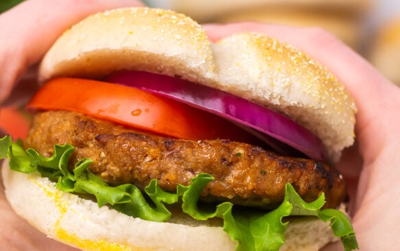 close up of turkey burger topped with lettuce, tomato, and red onion.