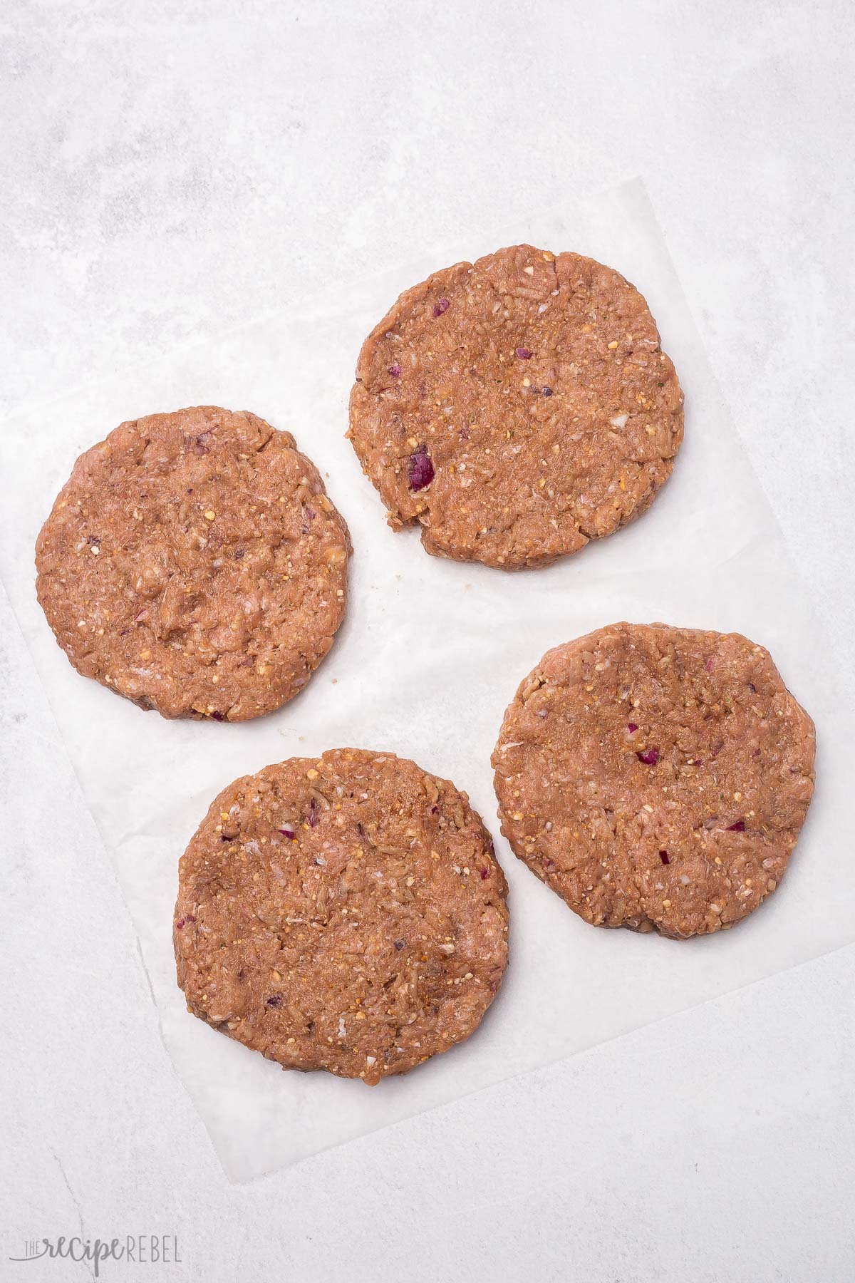 four formed turkey burgers, raw and lying on parchment paper.