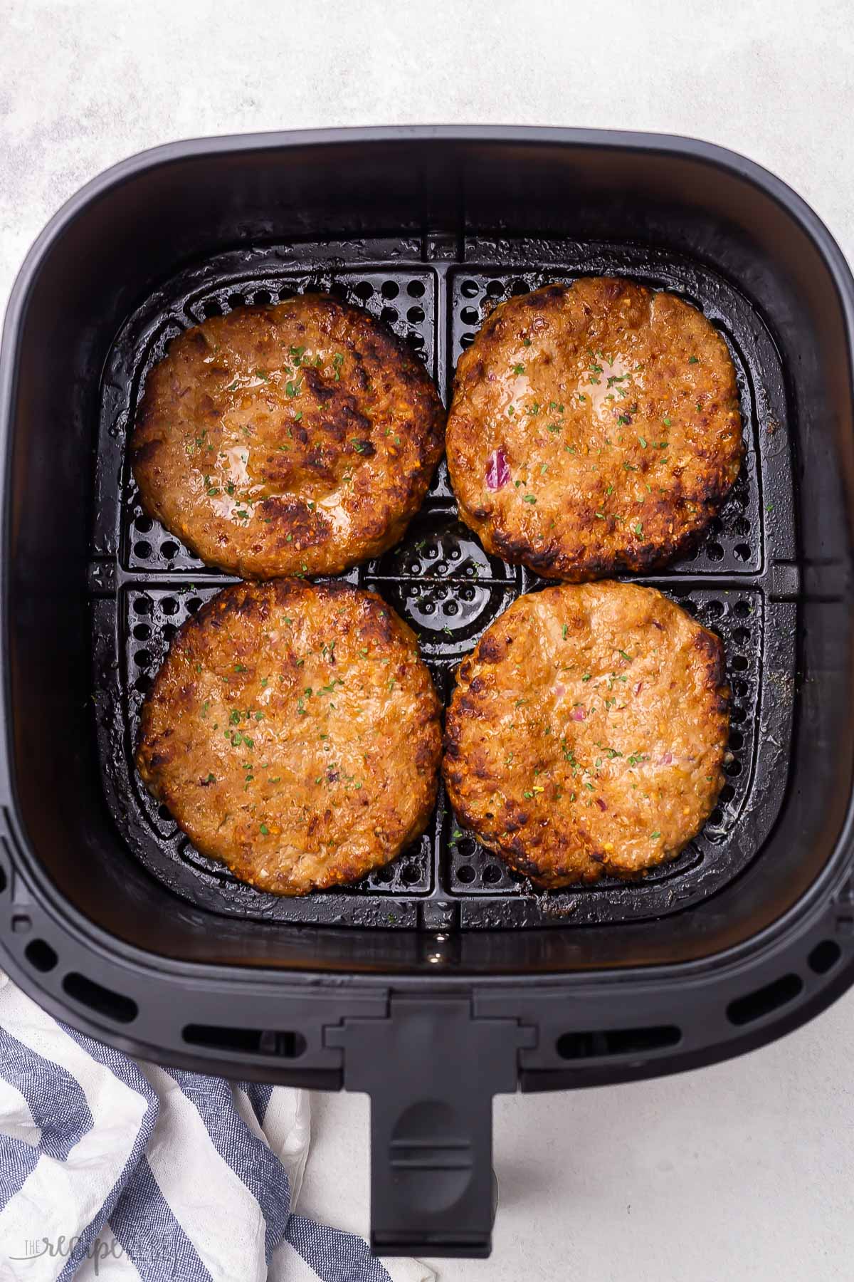 overhead shot of four cooked turkey burgers in air fryer basket.