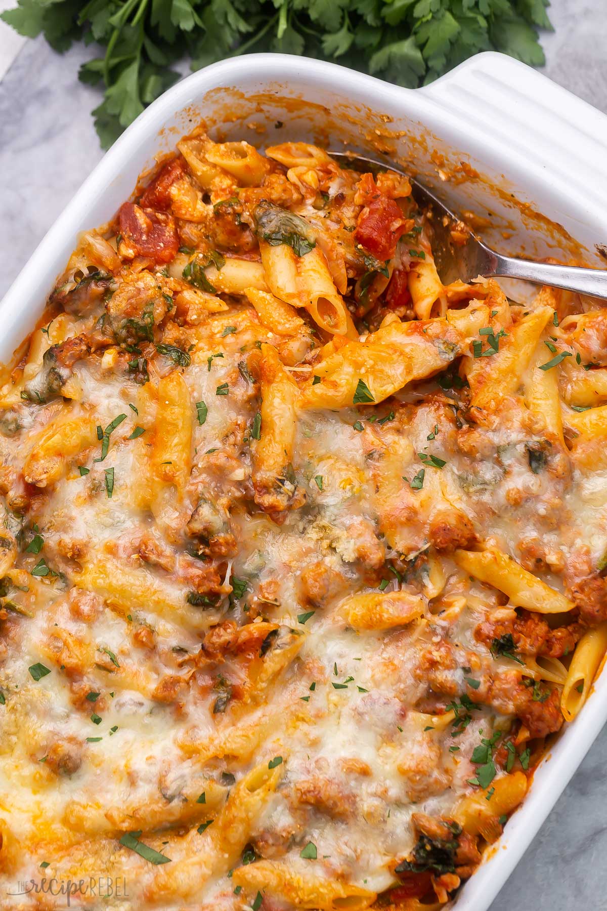 close up of serving spoon lying in pan of baked mostaccioli pasta.