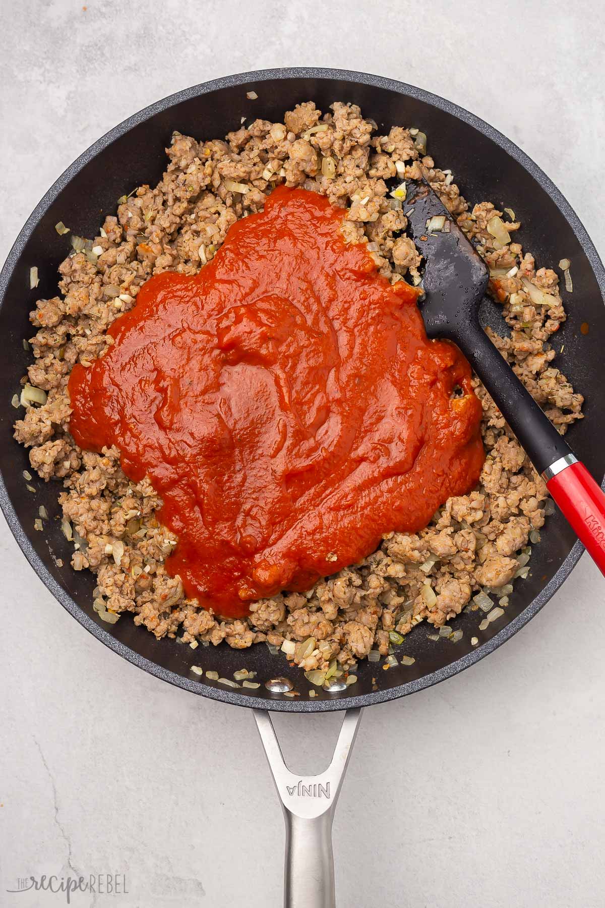 top view of meat, spices, and pasta sauce in black frying pan.