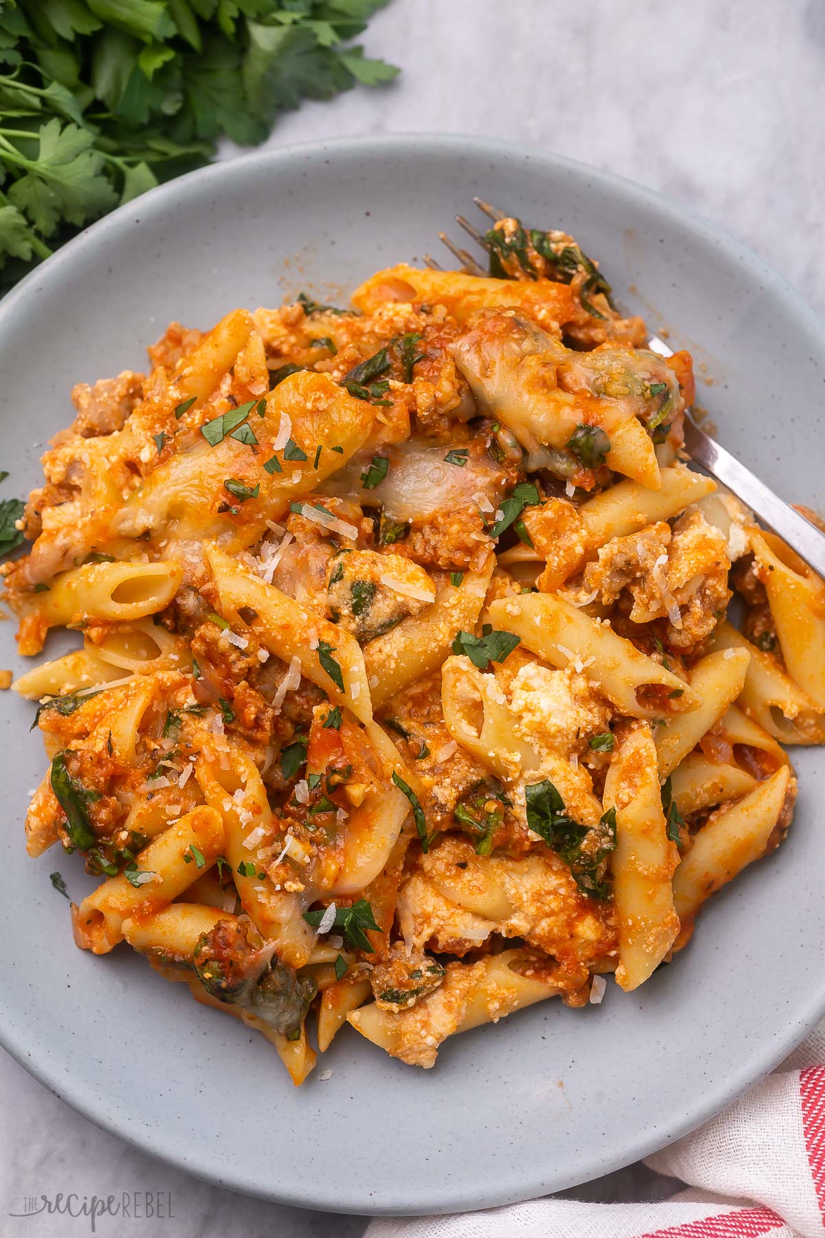 a fork on a grey plate full of baked mostaccioli pasta.