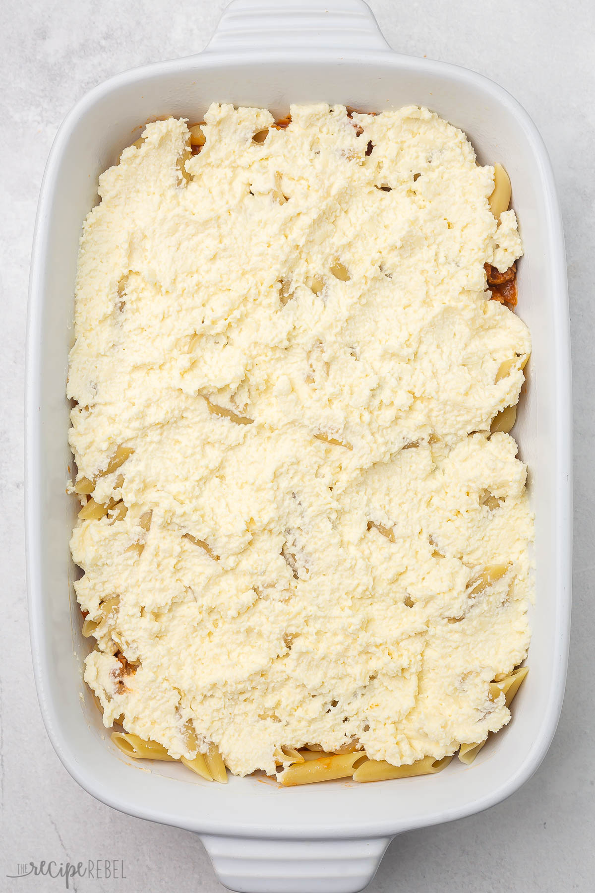 overhead view of baked mostaccioli pasta with ricotta mixture spread on top.