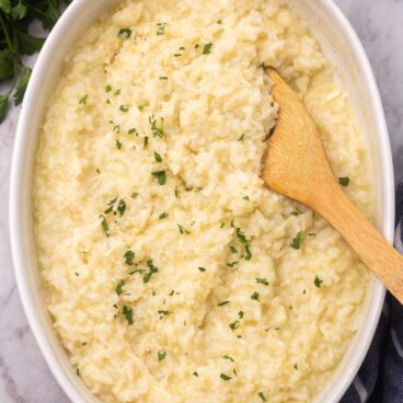 Top view of baked risotto in a dish with garnish on it and a wooden spoon in it.