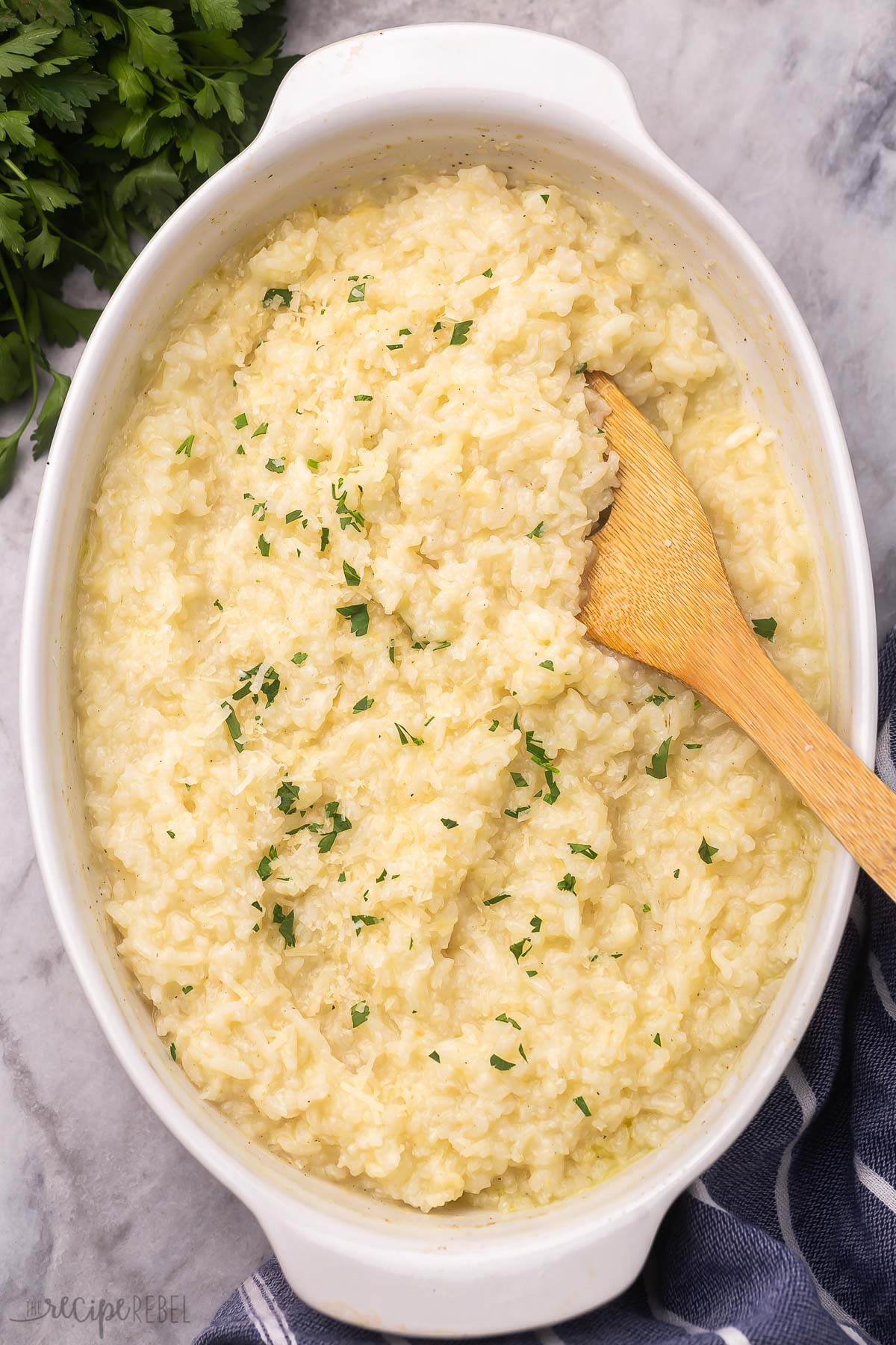 Top view of baked risotto in a dish with garnish on it and a wooden spoon in it.