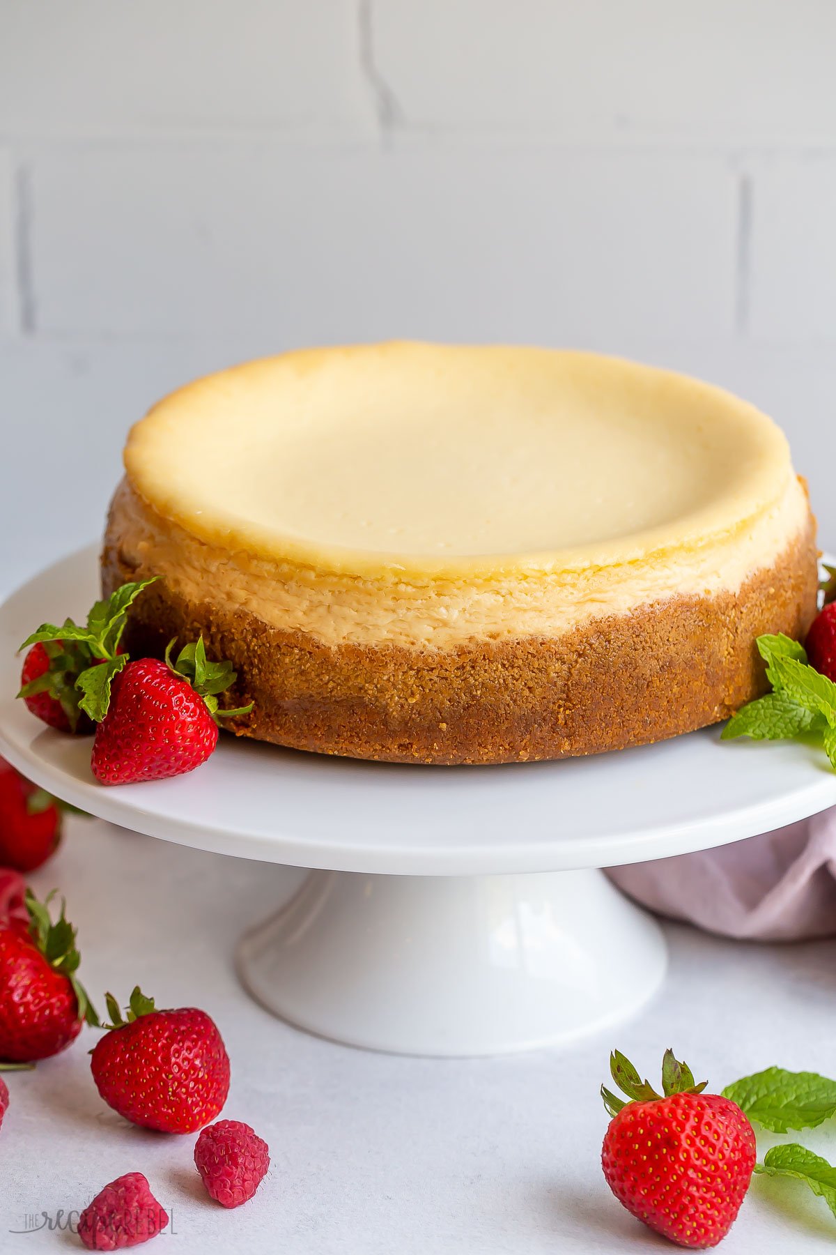 whole baked vanilla cheesecake on cake plate with berries around.