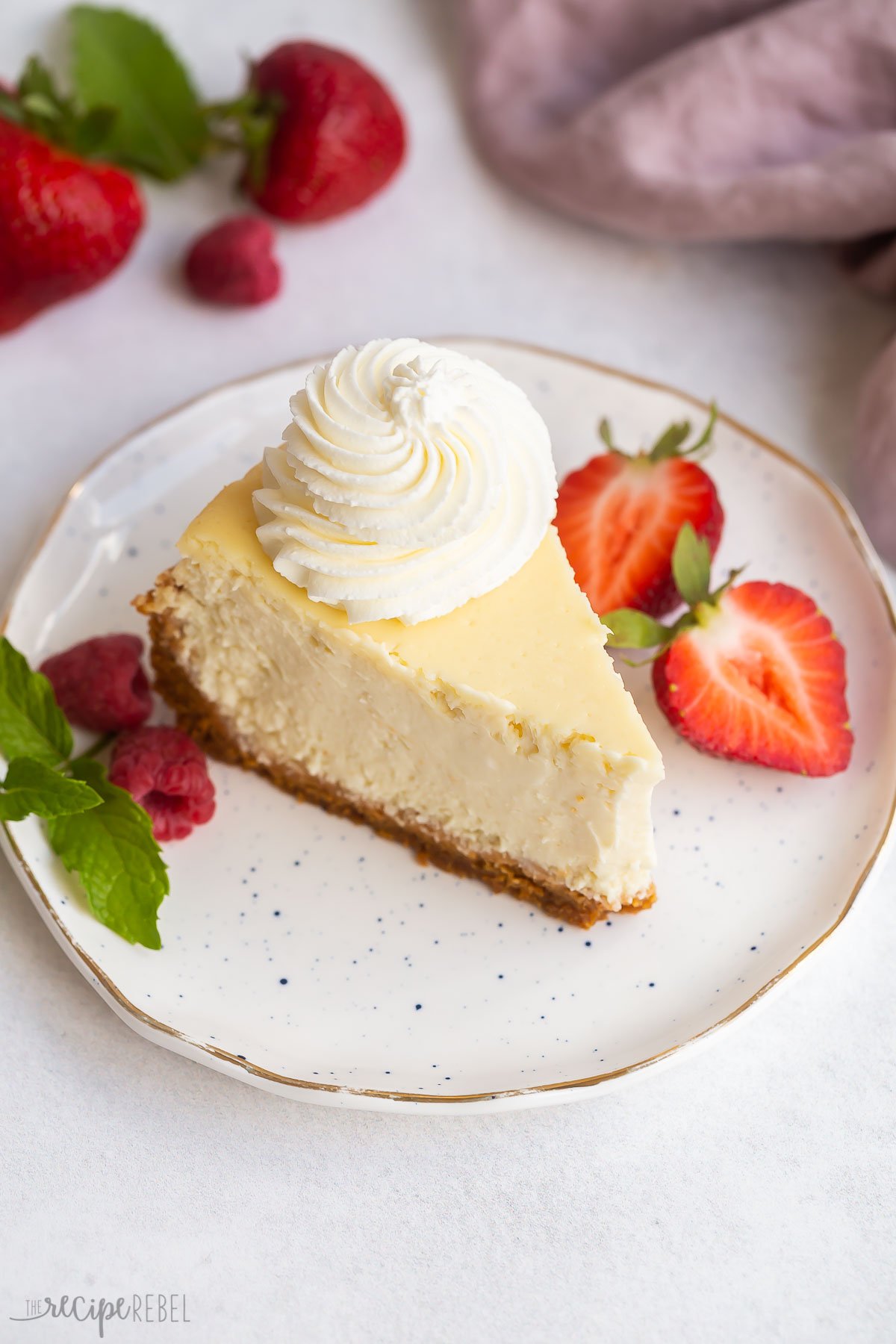 slice of baked vanilla cheesecake with whipped cream and berries on white plate.