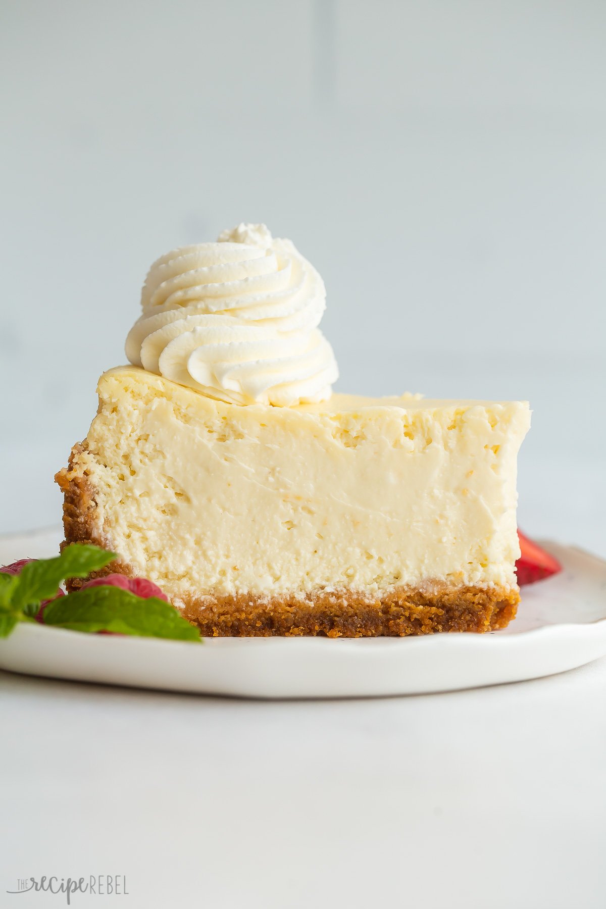 slice of baked cheesecake on white plate with whipped cream on top.