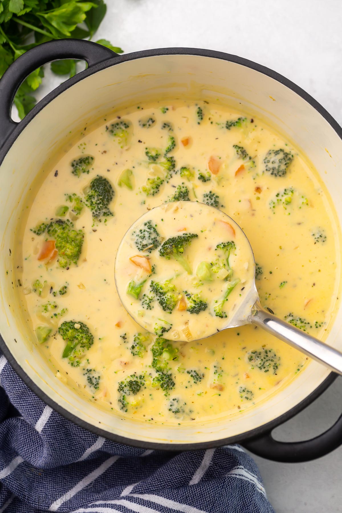 Top view of a full pot of broccoli cheddar soup with steel ladle scooping soup.