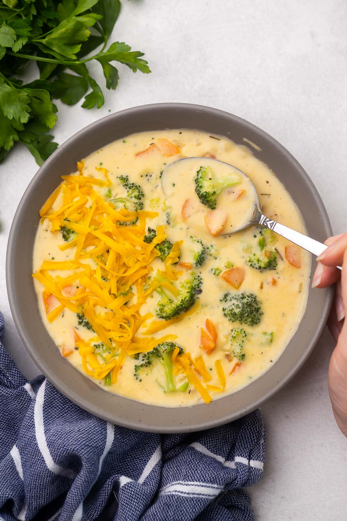 Top view of a bowl full of broccoli cheddar soup with a spoon scooping some out. 