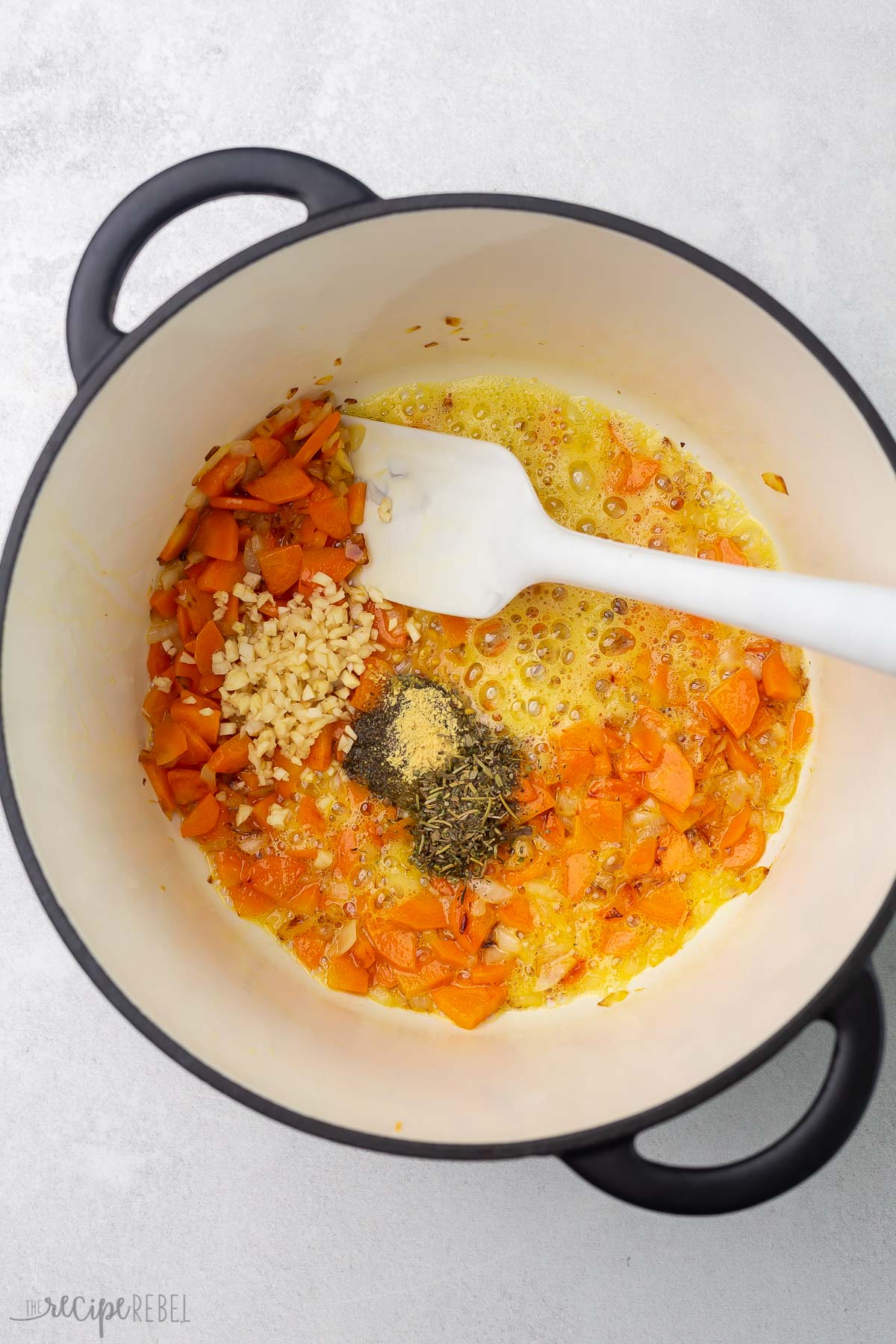 top view of pot with vegetables, spices, and white spatula.