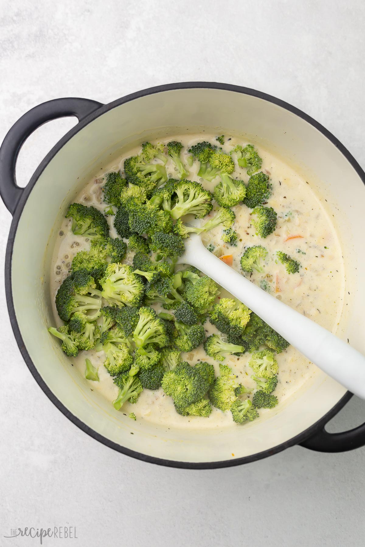 overhead view of soup ingredients in pot with broccoli on top and white spatula.