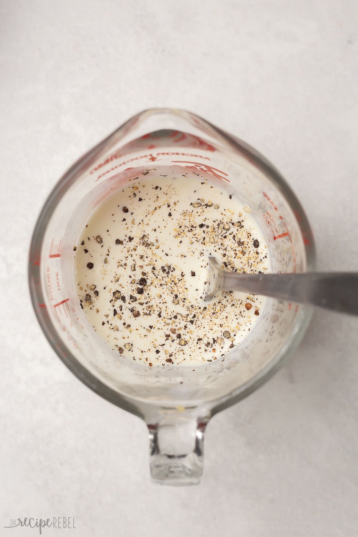 glass measuring cup with cream, spices, and a spoon in it.