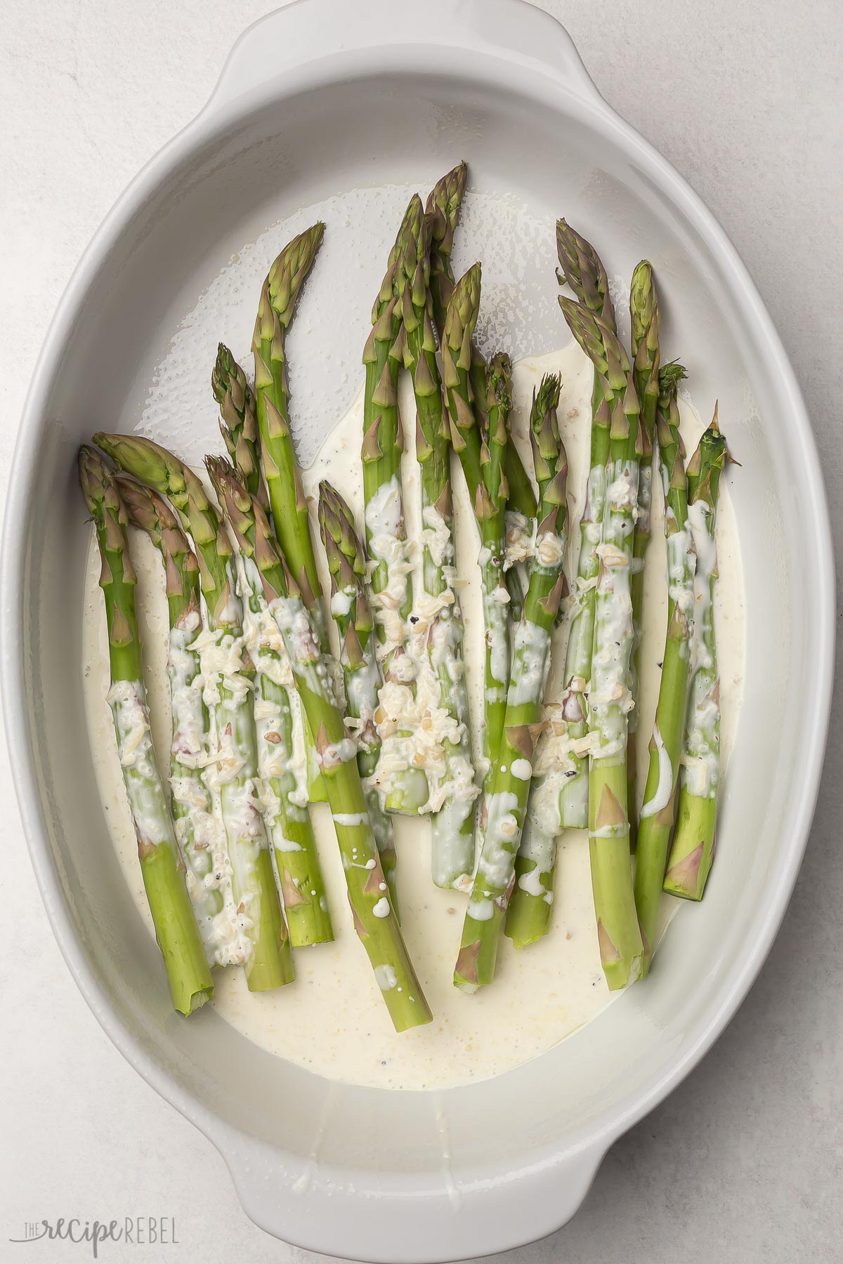 white baking dish with asparagus covered in cream sauce.