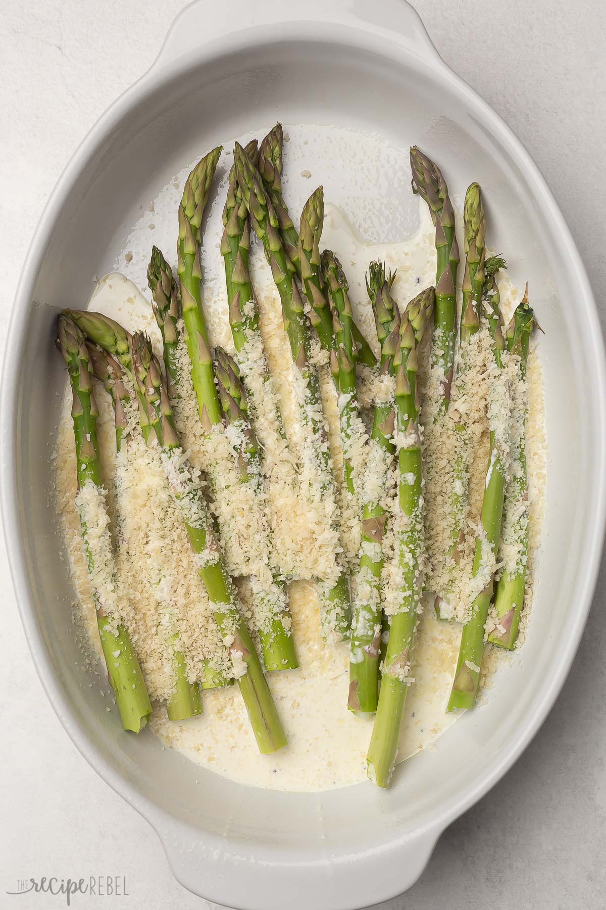 asparagus topped with parmesan cheese in white baking dish.
