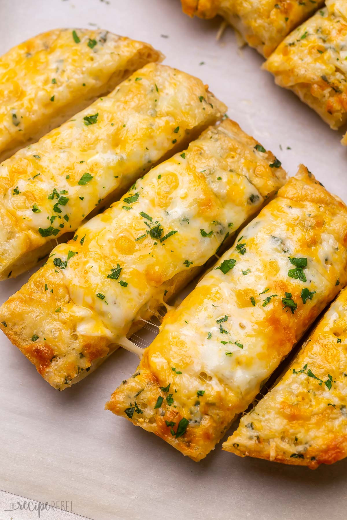 Top view of sliced cheesy garlic bread on a tray with chopped parsley sprinkled on top.