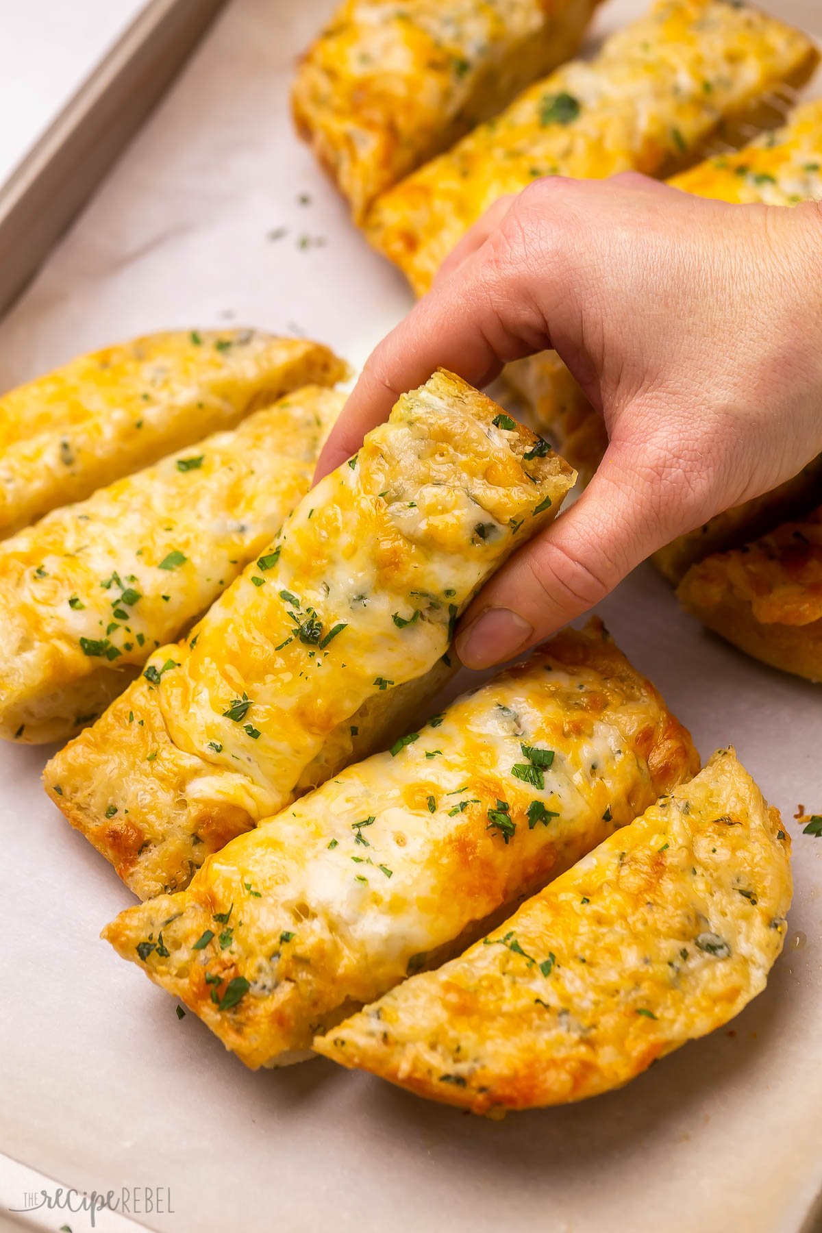 Close up of a piece of cheesy garlic bread being lifted off a baking pan.