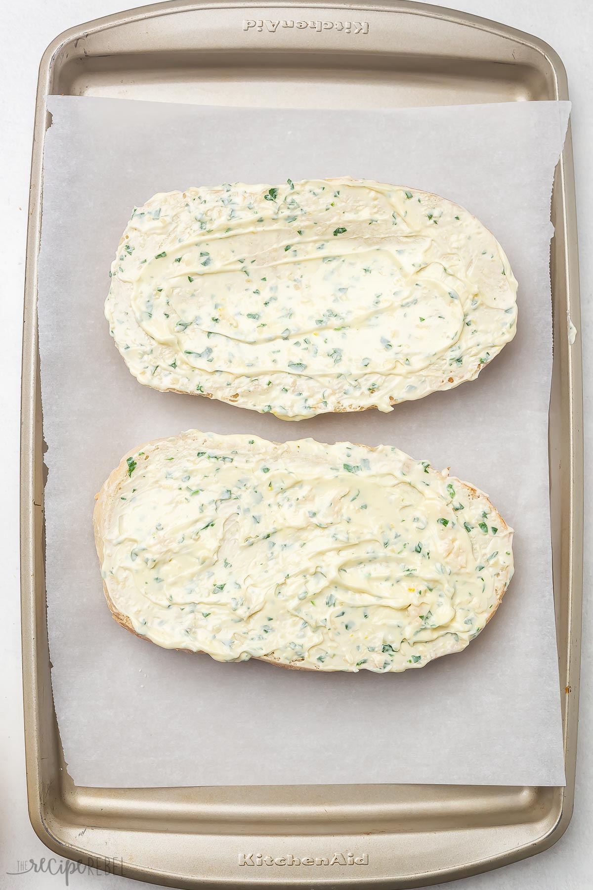 two loaves of buttered cheesy garlic bread on a pan with parchment paper.