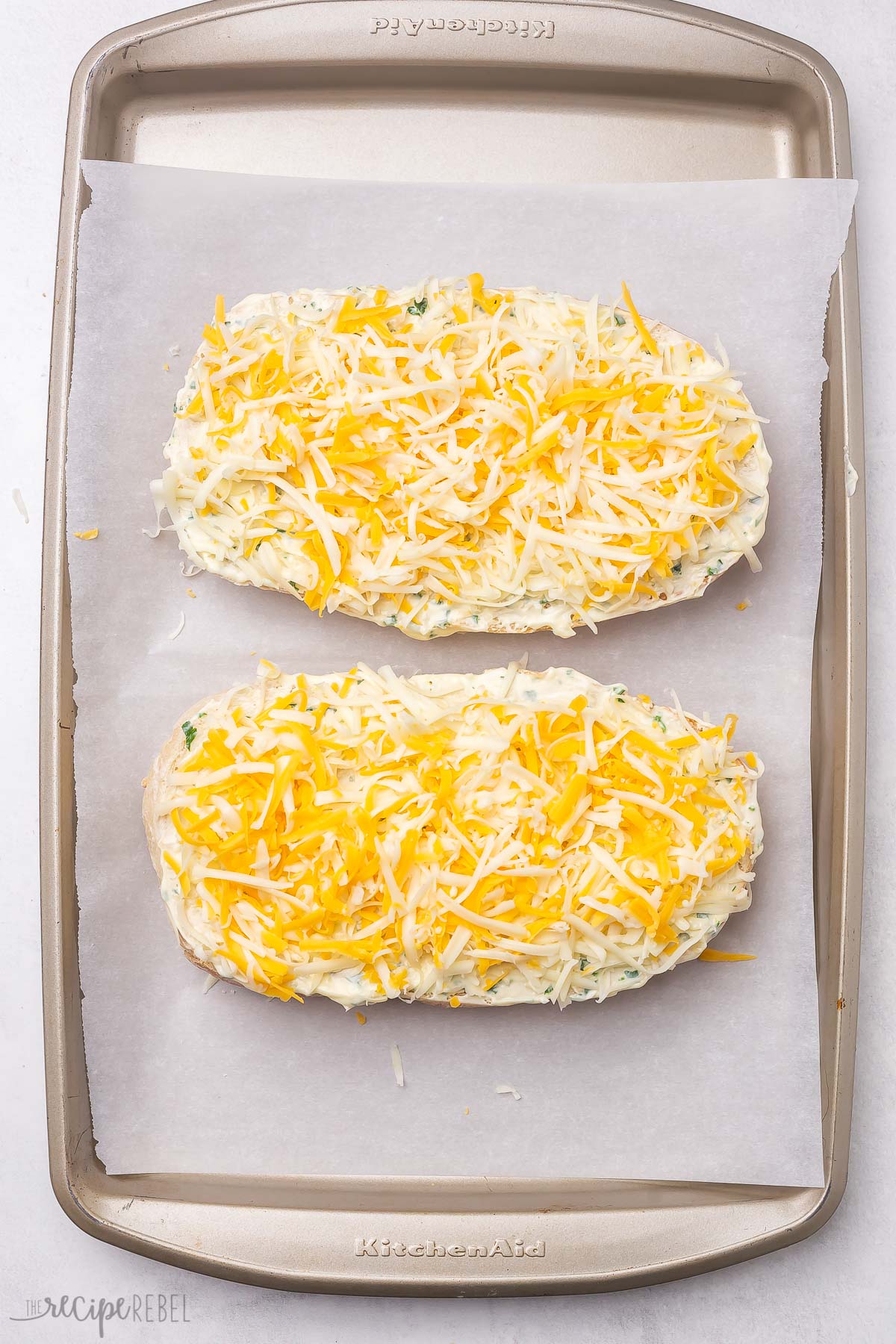 two loaves of cheesy garlic bread topped with cheese on a pan.