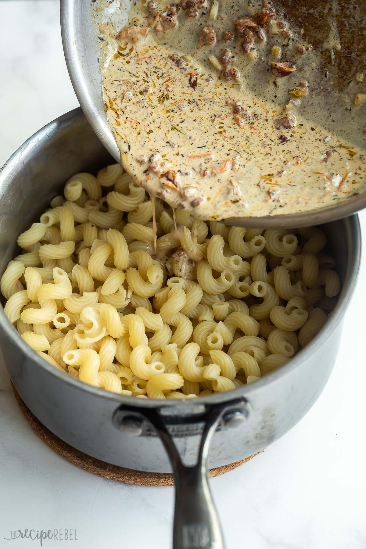 sauce being poured over pasta in stainless steel pot.