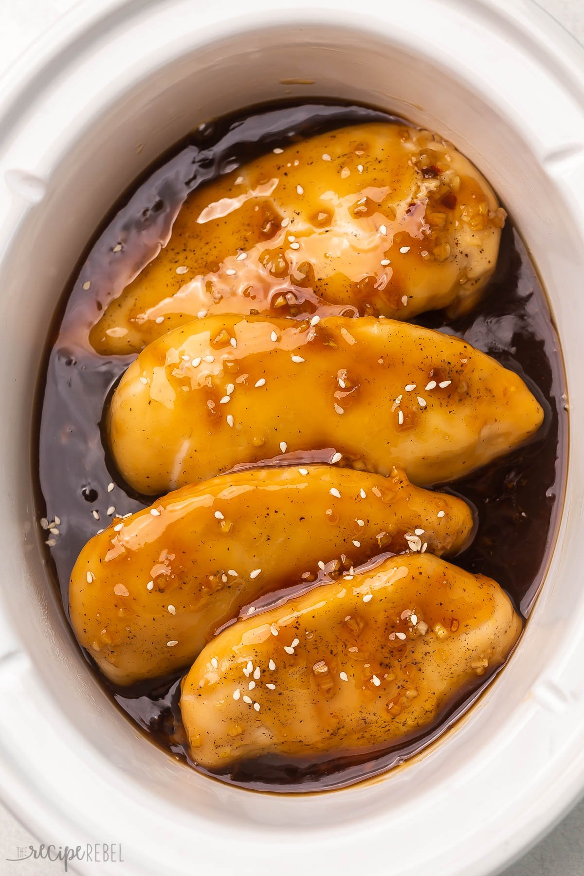 white crockpot with four chicken breasts and honey garlic sauce.