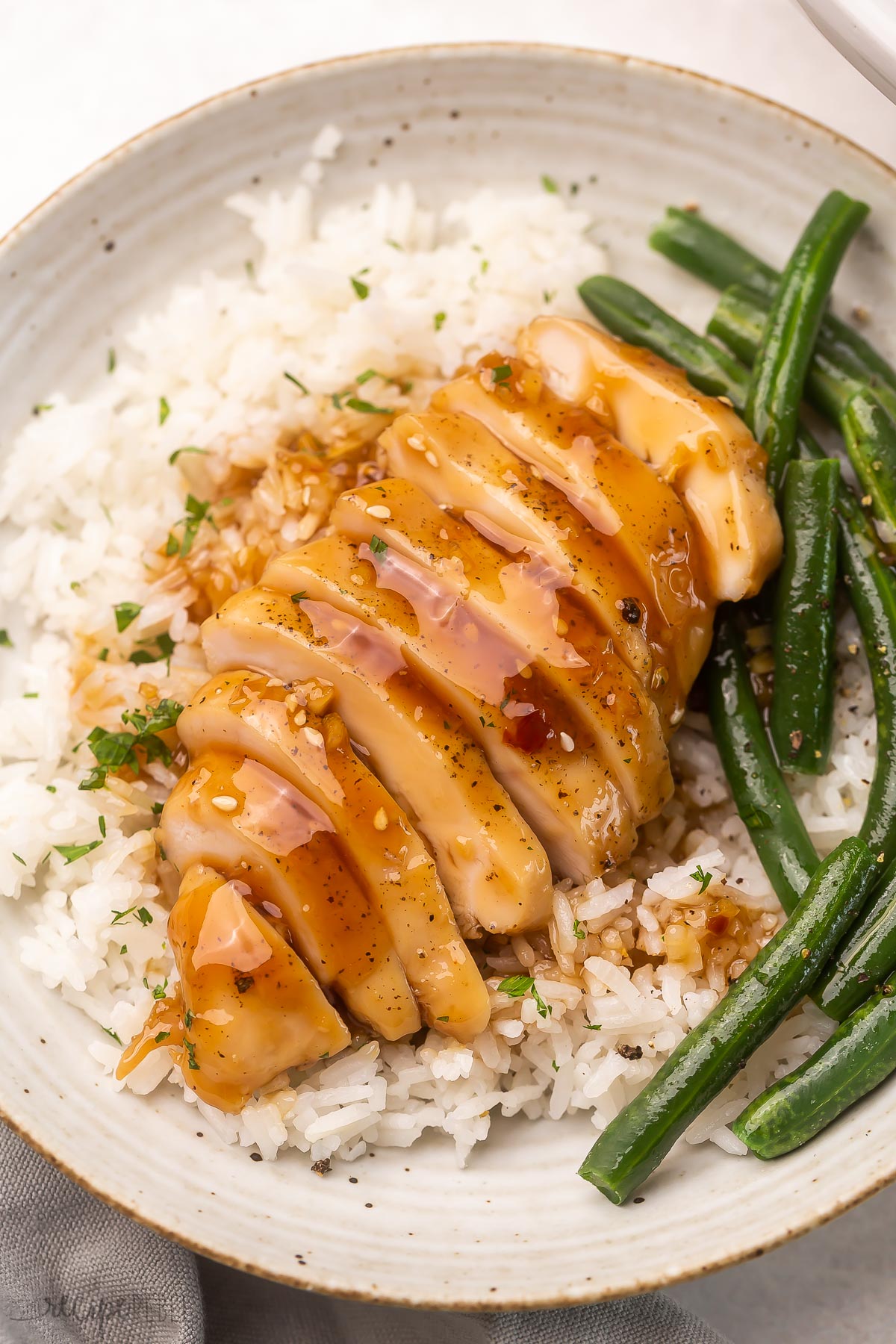 Close-up top view of a plate of rice topped with sliced honey garlic chicken and green beans.