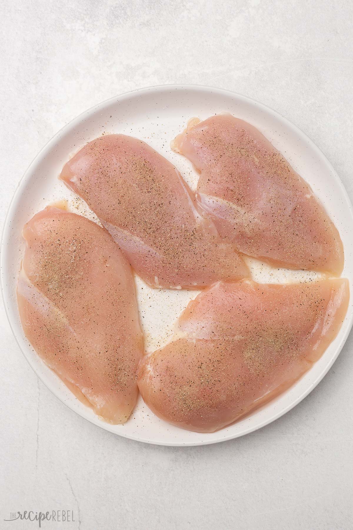 four seasoned chicken breasts on a white plate.