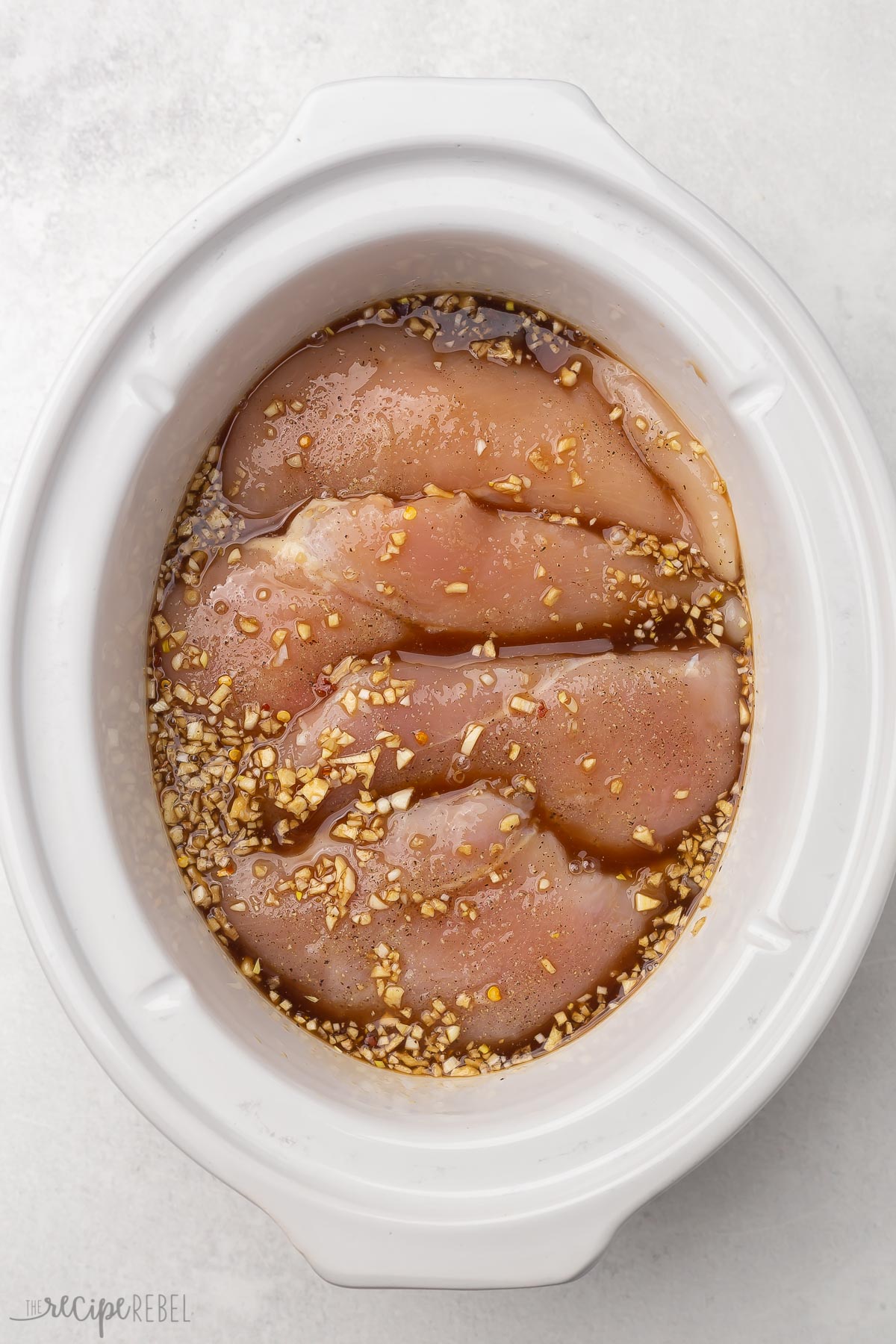 white crockpot with uncooked chicken breasts and honey garlic sauce.