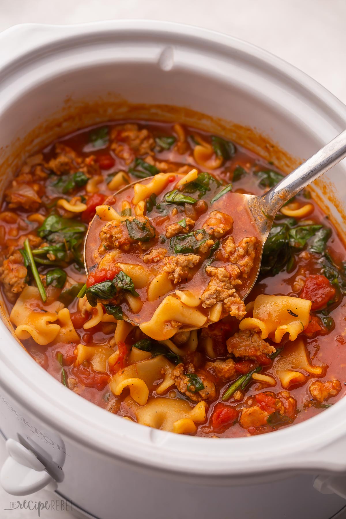 a steel ladle scooping crockpot lasagna soup out of white crockpot.