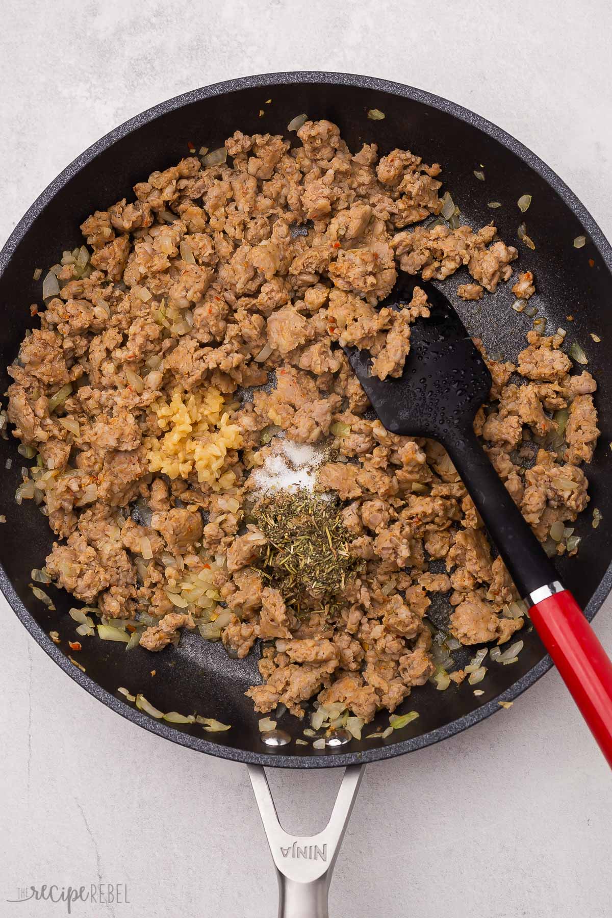 cooked meat in frying pan with spices placed on top and spatula in pan.
