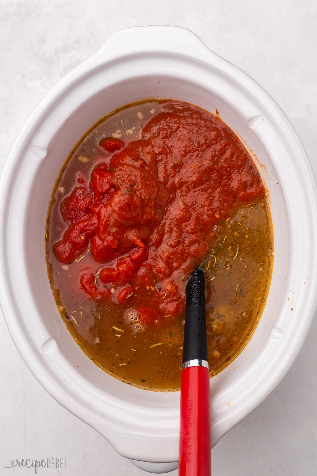 overhead shot of white crockpot with spatula and ingredients in it.