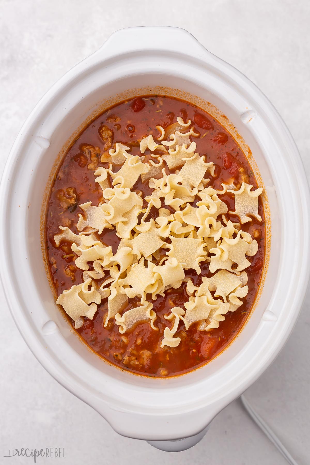 white crockpot with lasagna soup in it and broken lasagna noodles on top.