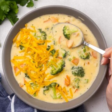 Top view of a bowl full of broccoli cheddar soup with a spoon scooping some out.