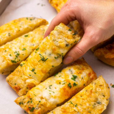 Close up of a piece of cheesy garlic bread being lifted off baking pan.