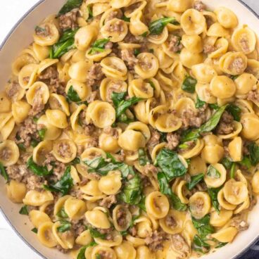 overhead view of orecchiette pasta and sausage in white pot.