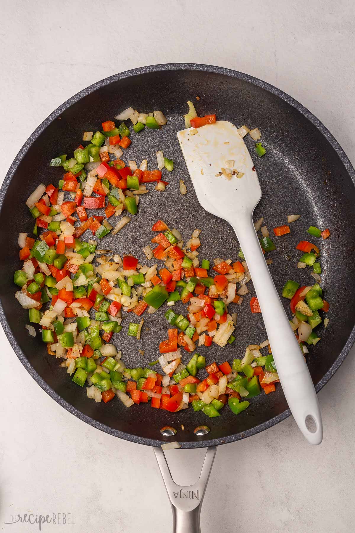 peppers and onions in a black frying pan with a white spatula.