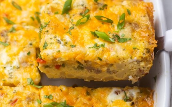 close up of a piece breakfast casserole being lifted out of white dish.