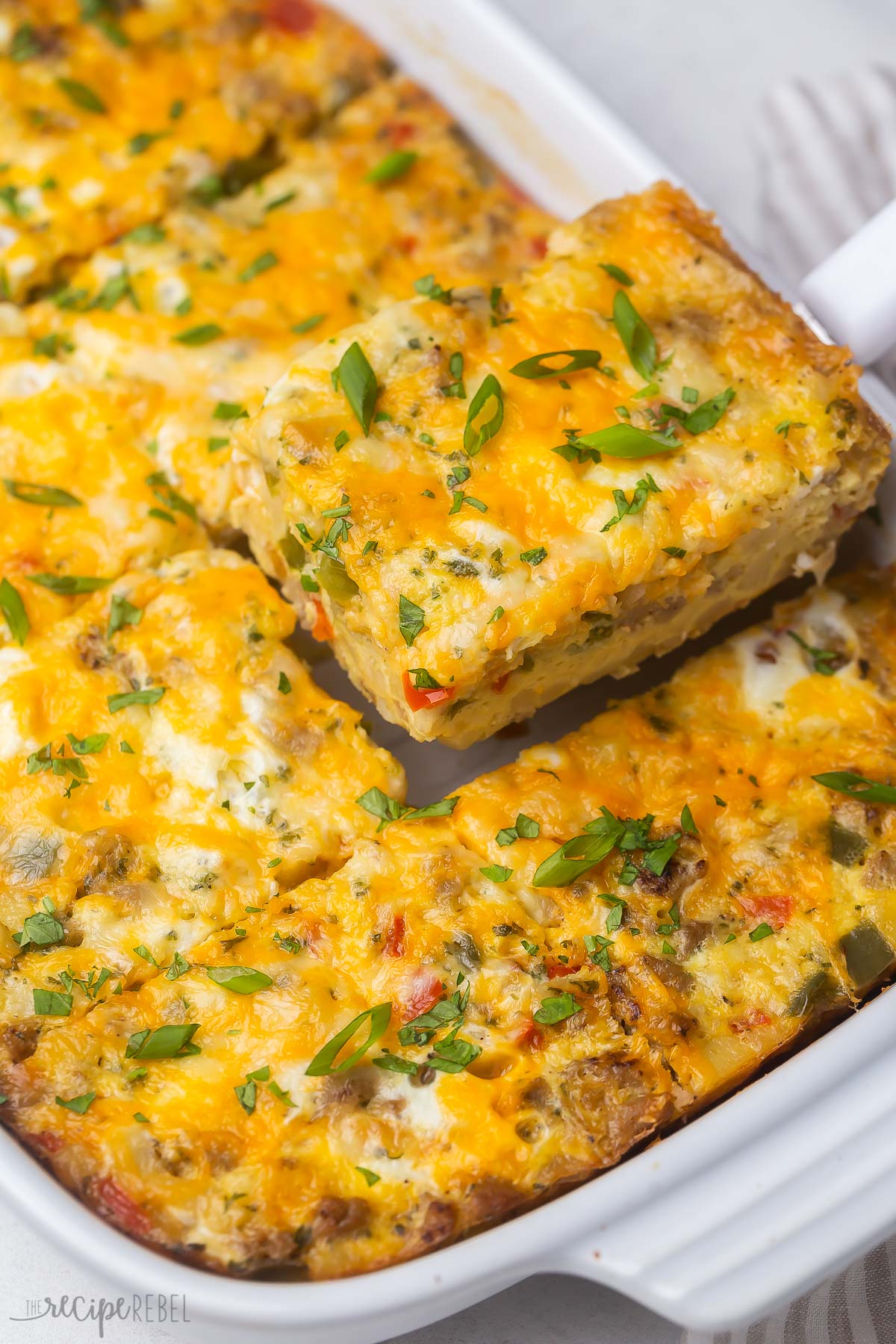 a piece of hashbrown breakfast casserole being lifted out of a white pan.