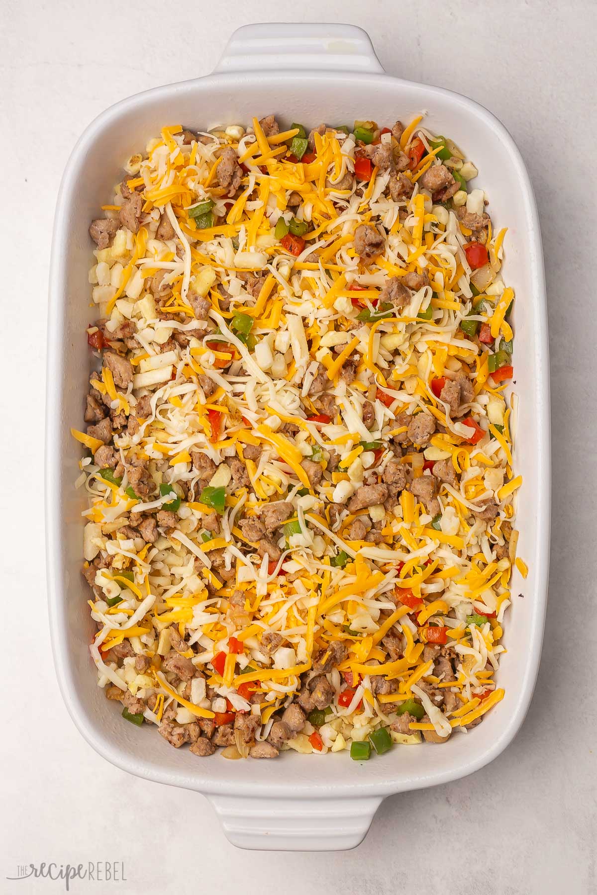 hashbrowns, sausage, vegetables, and cheese in white baking dish.